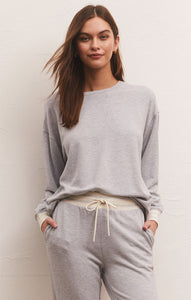 Light grey modal crewneck pullover with ivory & grey stripe cuff details. Being worn by a woman in front of a white background. Hands in both pockets showcasing the comfortability of this sweatshirt.