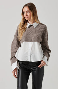 A woman wearing a mixed media top. It is a brown taupe sweater with a white button down underneath that comes as one piece. Classic collared shirt. She paired it with a faux leather high waisted pant.