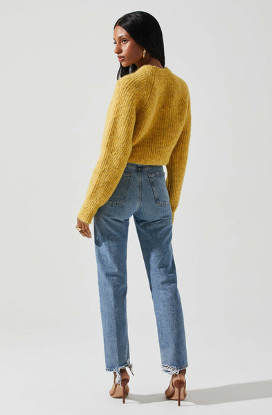 A woman in front of a white background wearing a yellow knit sweater. This sweater is a beautiful mellow yellow with two front cutouts. She paired it with a high waisted medium wash denim, brown belt & gold jewelry. She is also wearing a simple brown high heel.