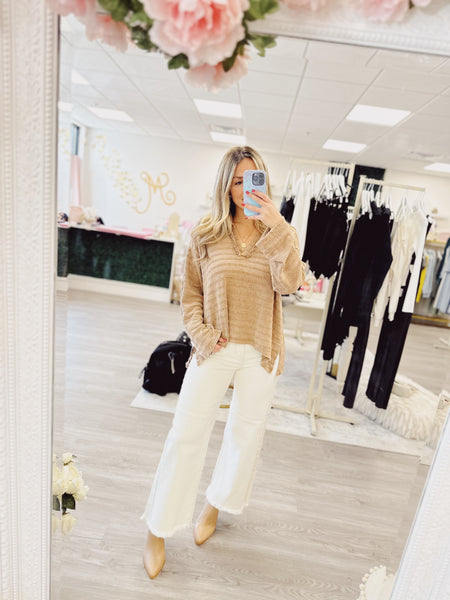 Cream wide leg frayed hem pant being worn by a woman in a boutique store location with a neutral background. Paired easily with a light mocha brown textured v-neck long sleeve with a oversized slouchy fit. 