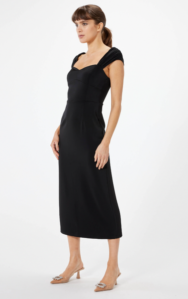 A woman in front of a white background wearing a black midi dress with cap sleeves and a sweetheart neckline. Back high slit to give a sleek look to this simple yet classic dress. Wearing her hair up in a ponytail and classic point toe high heels