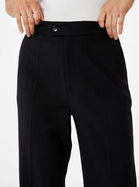 A woman wearing a black trouser pant with pockets and front zipper & button in front of a white background.
