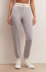 Light grey modal soft jogger with ivory elastic waistband and tie. Being worn and modeled on a woman with a white background and white sneakers with high ankle white socks. 